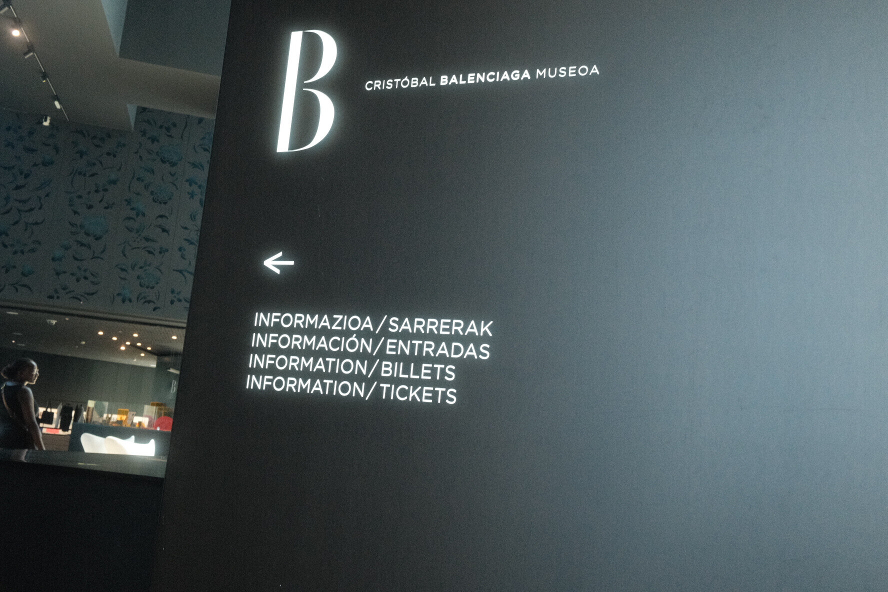 Black museum sign with a large letter B reading Cristobal Balenciaga Museoa, arrow pointing left.