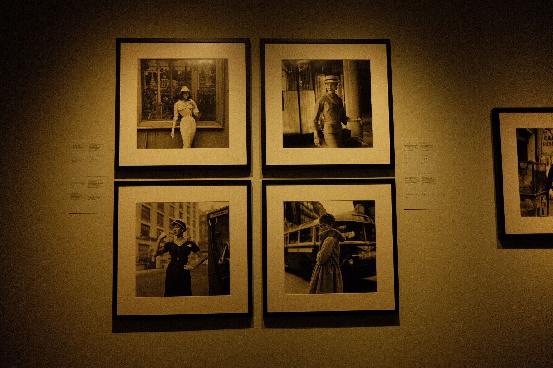 Four framed black-and-white fashion photographs in a grid on a dim gallery wall.